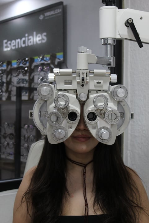 Person wearing a white phoropter eye exam device with multiple lens wheels in an optometry clinic
