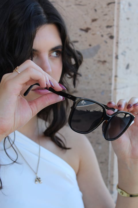 Woman with dark hair holding black sunglasses